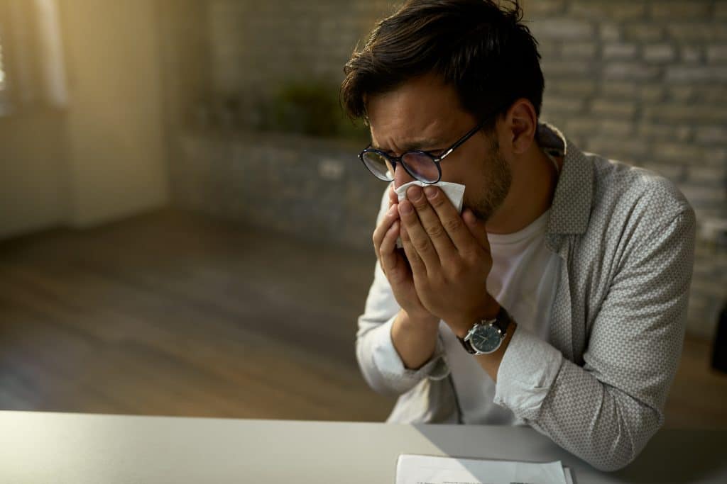 young businessman feeling sick and blowing nose while working in the office