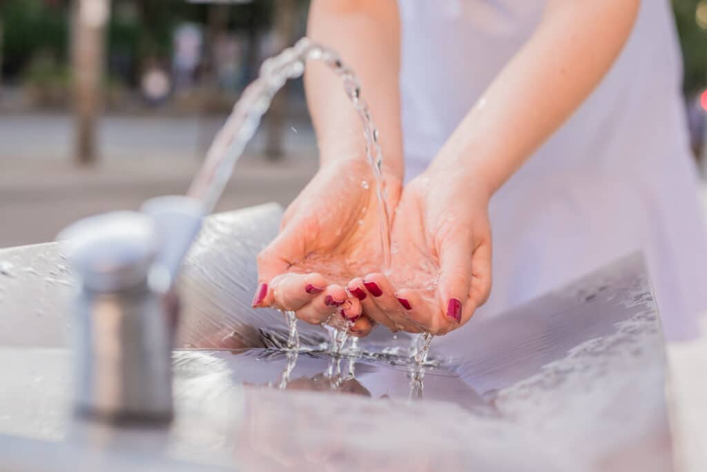 closeup woman hand catching water splashing drops sunny summer outdoors background environment health concept flowing fountain cool drink